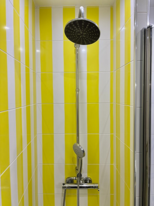 Baño moderno con alcachofa de lluvia negra y ducha de mano contra azulejos a rayas amarillas y blancas en París