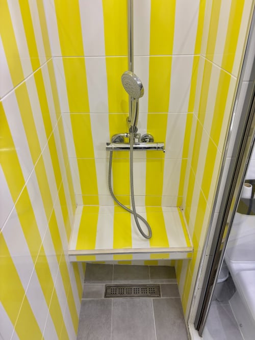 Moderno baño con azulejos a rayas amarillas y blancas, cabezal de ducha portátil y accesorios cromados en Aldaro Paris