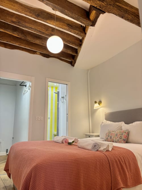 Dormitorio acogedor en apartamento parisino de Odéon Saint Germain con vigas de madera rústica, colcha coral y comodidades modernas