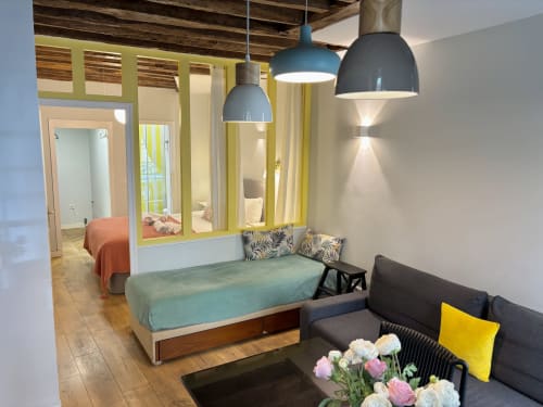 Dormitorio de apartamento parisino moderno con cama, sofá, lámparas colgantes y distribución abierta en ALDARO Odéon Saint Germain