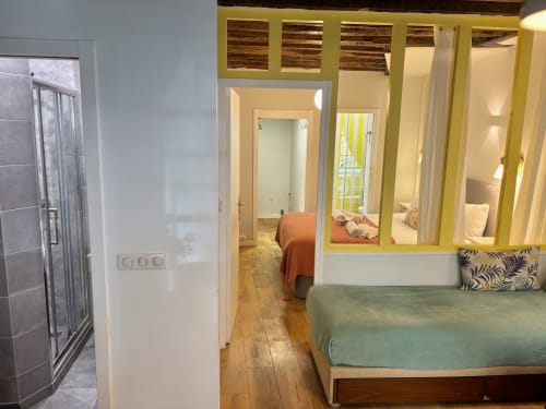Dormitorio de apartamento parisino moderno con cama verde, puertas-ventanas de marco amarillo, baño privado, piso de madera