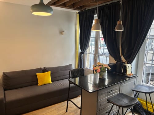 Sala de estar de apartamento parisino moderno con sofá negro, cojín amarillo, mesa de comedor negra y lámparas colgantes