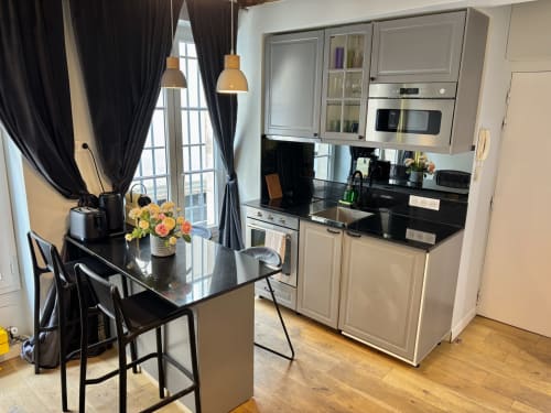 Cocina moderna con encimeras negras, armarios blancos y zona de comedor en el apartamento Aldaro París