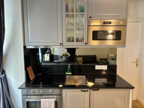 Cocina moderna del apartamento Aldaro Paris con encimeras negras, gabinetes blancos, electrodomésticos de acero inoxidable y acabados oscuros