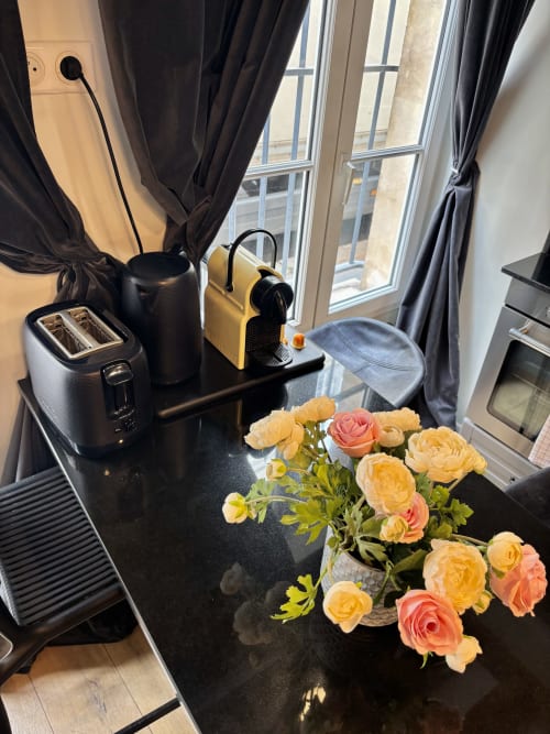 Cocina de apartamento parisino moderno con cafetera amarilla, tostadora, hervidor y rosas melocotón frescos junto a la ventana