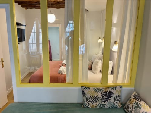 Dormitorio con tabique acristalado en apartamento parisino con marcos amarillos, camas con almohadas blancas y cojines estampados