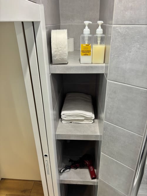 Estantería de baño empotrada con artículos de tocador, toallas y secador de pelo en el apartamento Aldaro París