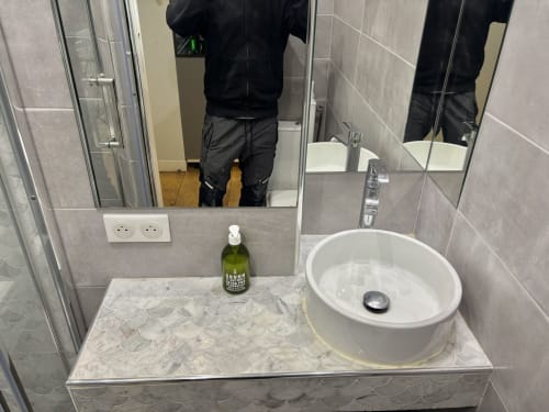Vanidad de baño moderno con lavabo redondo en apartamento Aldaro Paris, diseño de azulejos grises con amenidades