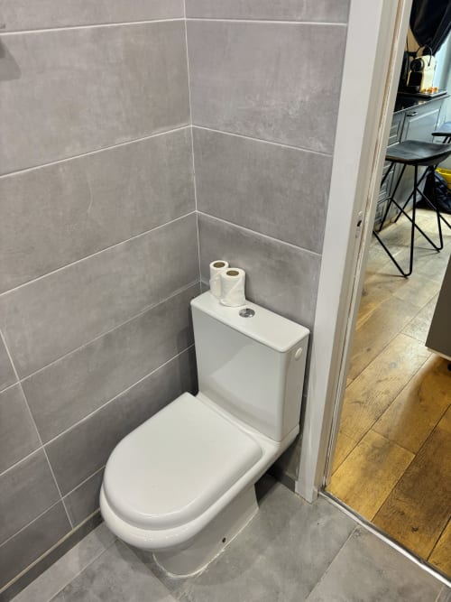 Inodoro blanco moderno con paredes de azulejos grises en el baño del apartamento Aldaro, París