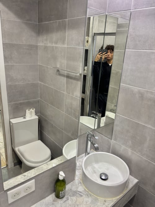 Baño moderno del apartamento Aldaro Paris con azulejos grises, lavabo blanco redondo, inodoro y espejo grande