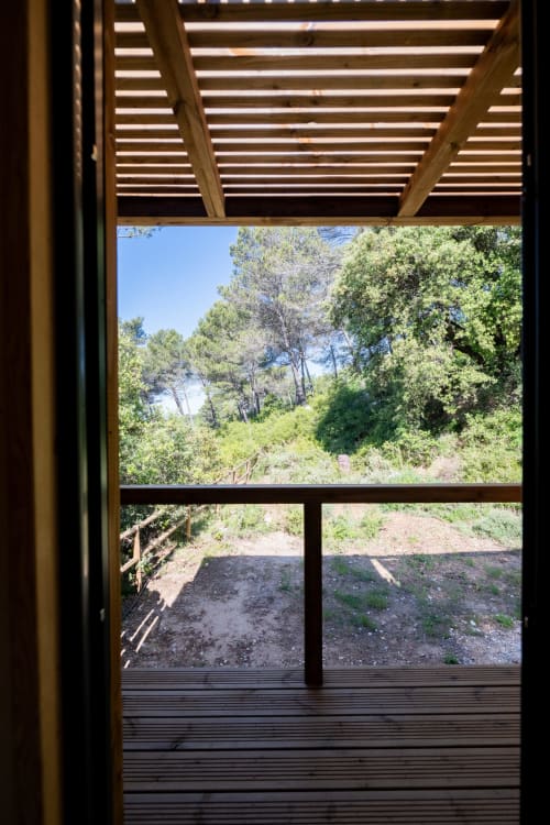 View from Le chant des pins lodge cottage showing wooden pergola, terrace, and forested hillside with trees