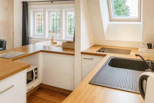 Cuisine moderne de la Suite Maunoury à Maunoury Citybreak, Chartres, avec plans de travail en bois, mobilier blanc et vue sur le jardin