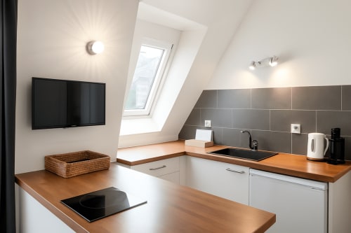Kitchenette de suite mansardée moderne à l'hôtel Maunoury Citybreak à Chartres avec comptoirs en bois, armoires blanches et puits de lumière