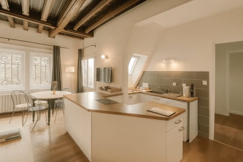 Cuisine-séjour de la Suite Moderne Maunoury à l'hôtel de Chartres avec mobilier blanc, poutres apparentes et vue sur le jardin