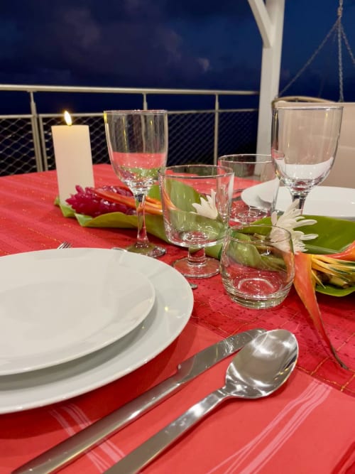 Élégant dîner en bord de mer à Villa Chanté Grenouilles avec nappe rouge, assiettes blanches, fleurs tropicales et océan