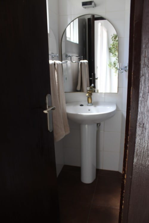 Baño moderno con lavabo de pedestal, espejo redondo y toallero en habitación de Villa Palmer hostel, Paguera