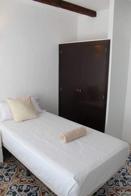 Habitación doble moderna en el hostal Villa Palmer de Paguera con cama blanca, almohada color crema, toalla enrollada y armario de madera oscura