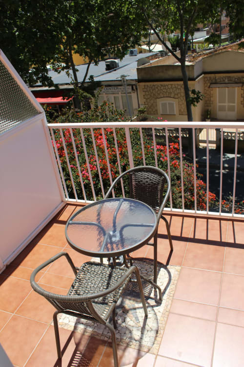 Zona de asiento sombreada en la terraza de la Villa Palmer en Paguera, con mesa, silla y plantas florecidas bajo la barandilla