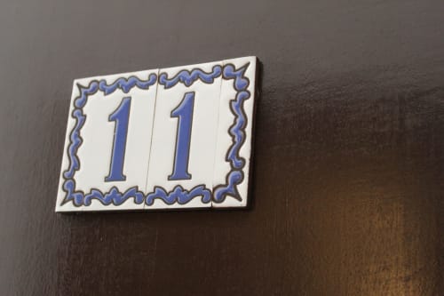Placa con número 11 en Villa Palmer hostel de Paguera, España. Azulejo cerámico azul con borde decorativo sobre pared oscura.