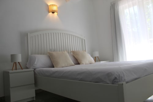 Dormitorio moderno y luminoso en Villa Palmer Paguera con cama blanca, almohadas beige, mesillas de noche y luz natural del balcón