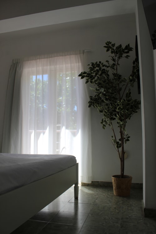 Habitación luminosa en Villa Palmer hostel de Paguera con cama, cortinas translúcidas, vista al balcón y maceta