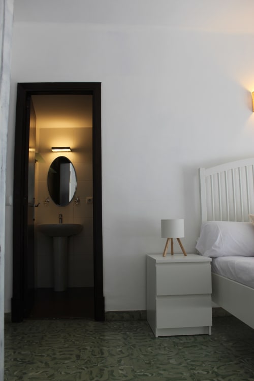 Habitación moderna en Villa Palmer hostel de Paguera con baño privado, cama blanca, mesita de noche con lámpara y marco negro