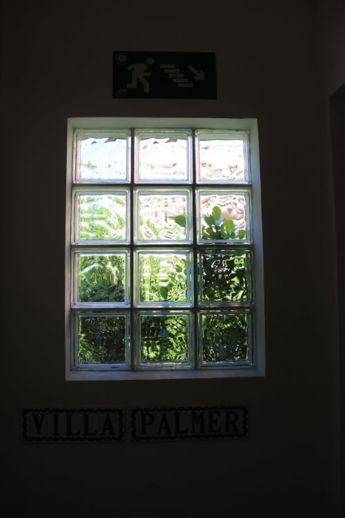 Ventana de bloques de vidrio con vista al jardín en Villa Palmer hostel de Paguera, mostrando exuberante follaje verde