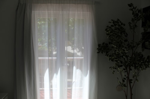Vista luminosa del balcón con cortinas translúcidas en Villa Palmer de Paguera, mostrando jardín y luz natural en habitación doble