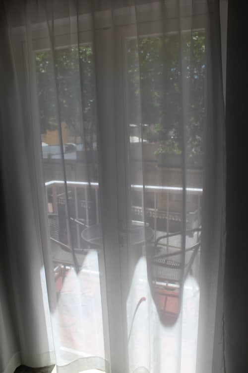 Cortinas blancas translúcidas enmarcando la vista del balcón en Villa Palmer hostel de Paguera, con jardín y zona de estar exterior
