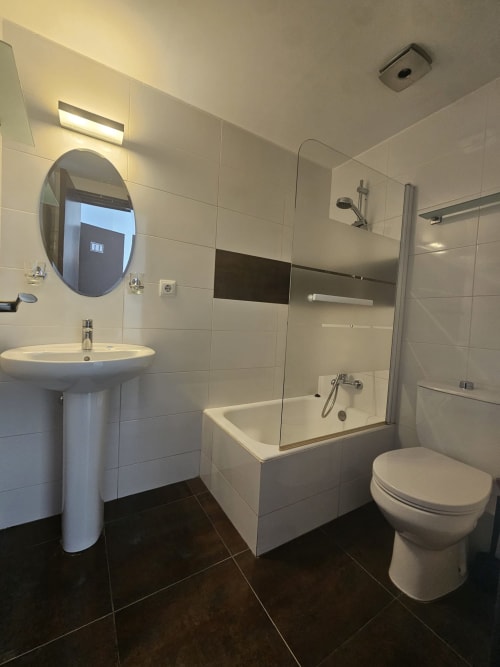 Baño moderno en Villa Palmer hostel en Paguera con espejo redondo, lavamanos pedestal, inodoro y ducha de cristal