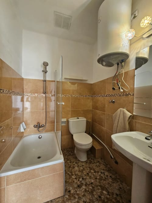 Baño moderno en hostel Villa Palmer, Paguera con azulejos de terracota, bañera con ducha, inodoro, lavabo y toallero calefactor