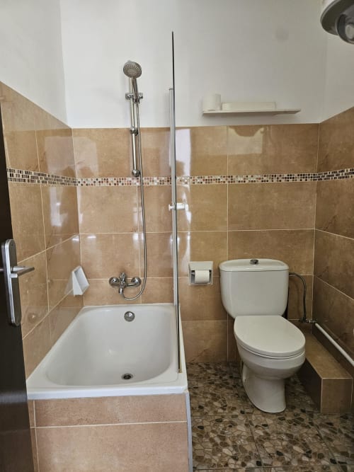 Baño moderno en el hostal Villa Palmer de Paguera con bañera, ducha, inodoro y paredes de azulejos beige