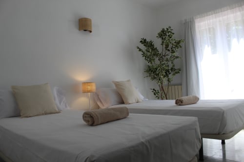 Dos camas individuales gemelas con ropa de cama beige, almohadas y toallas enrolladas en una habitación luminosa y minimalista del hostal Villa Palmer en Paguera