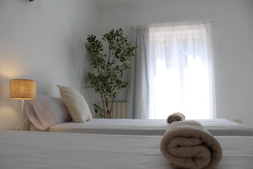 Luminosa habitación en el hostal Villa Palmer de Paguera con ropa de cama blanca, planta decorativa, lámpara cálida y cortinas traslúcidas