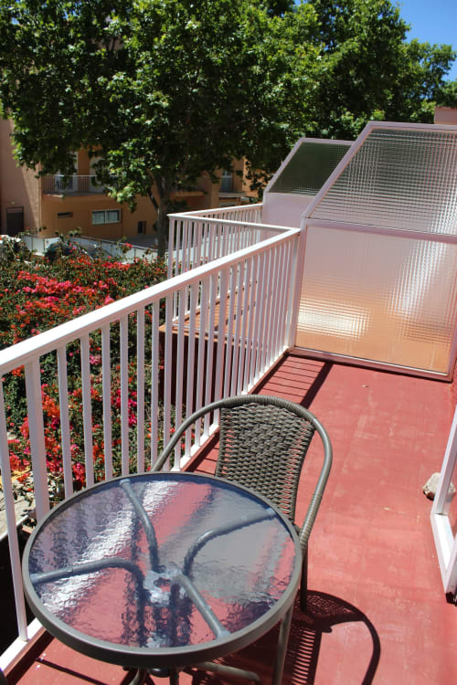 Balcón soleado de la Villa Palmer en Paguera con mesa de patio, silla de mimbre, barandillas blancas y jardines floridos abajo