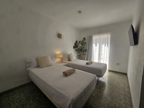 Habitación doble con dos camas en Villa Palmer hostel de Paguera con ropa de cama blanca moderna, TV y acceso a balcón