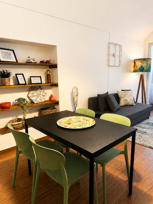 Sala de estar e jantar moderna com mesa preta, cadeiras verdes, sofá escuro, prateleiras de madeira e iluminação aconchegante