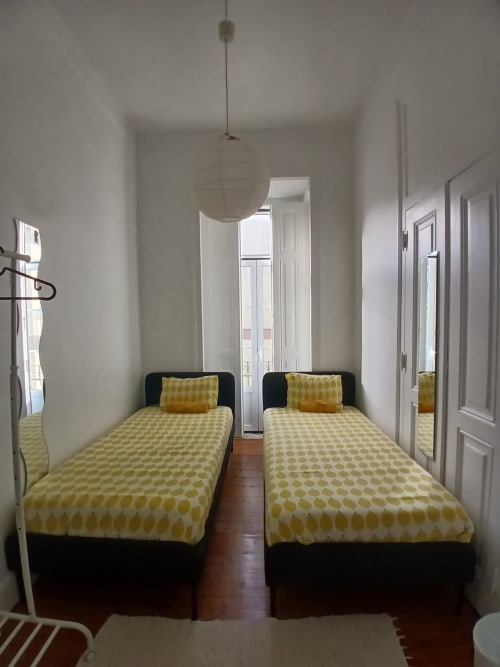 Quarto duplo no hostel Grupo Lisboa Alojamentos em Lisboa com roupa de cama amarela estampada e estruturas pretas