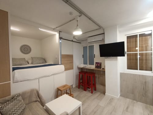 Moderno estudio en Sevilla con cama alta, cocina compacta, TV y mobiliario contemporáneo cerca del centro de metro