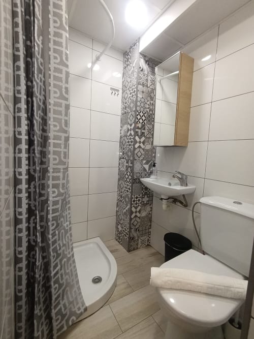 Baño moderno en apartamento El Rincón de Sevilla con azulejos blancos, pared con patrón decorativo, lavabo, inodoro, ducha y detalles de madera