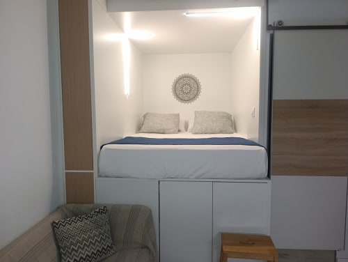 Acogedora alcoba con cama elevada, armarios de almacenaje, arte mandala en pared y zona de descanso en apartamento El Rincón de Sevilla