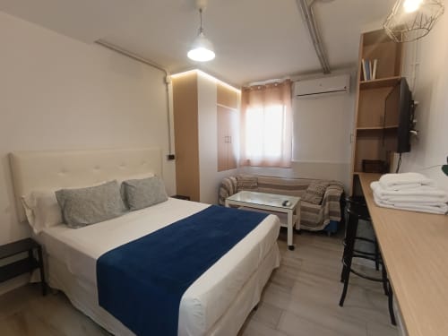 Moderno dormitorio en El Rincón de Sevilla con cama queen, sofá, TV y muebles de madera en Sevilla, España.