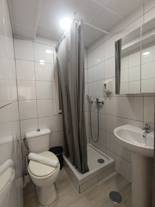 Baño moderno y limpio en el apartamento El Rincón de Sevilla con inodoro, lavabo, ducha y paredes de azulejos grises