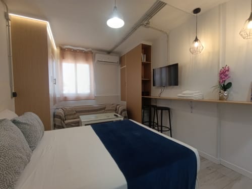 Moderno dormitorio de apartamento en El Rincón de Sevilla con cama doble, TV, sofá y cocina americana en Sevilla, España