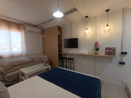 Habitación moderna en apartamento sevillano con vistas a la ciudad, televisor de pantalla plana, escritorio de trabajo, iluminación colgante y mobiliario contemporáneo