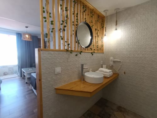 Baño moderno en apartamento estudio de Sevilla con tocador de madera, lavabo redondo y pared divisoria decorativa con plantas