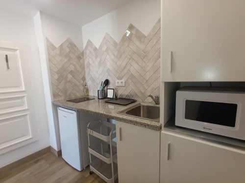 Cocina moderna en apartamento de Sevilla con azulejos tipo espiga, encimera de granito, fregadero de acero inoxidable y microondas