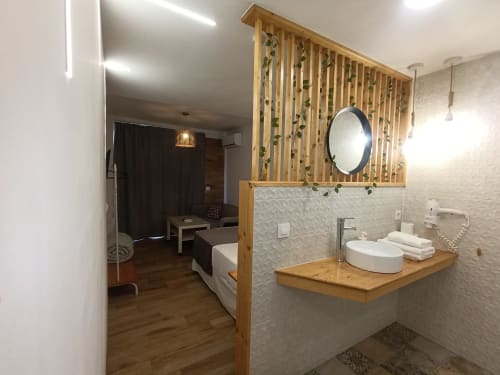 Baño de estudio moderno en El Rincón de Sevilla con vanitory de madera, espejo redondo, lavamanos de cerámica blanca y detalles decorativos