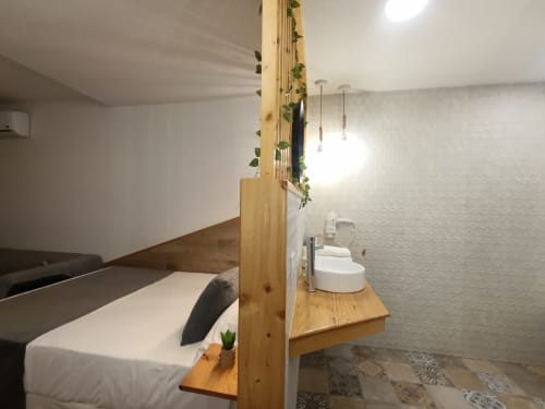 Moderno estudio en Sevilla con separador de madera, cama, lavamanos y lámparas colgantes