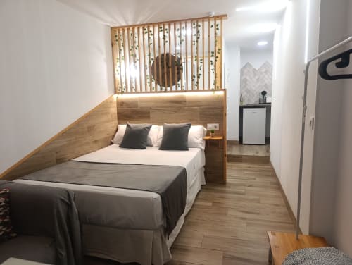 Moderno dormitorio de estudio en Sevilla con cama de madera, sábanas blancas y cocina americana con frigorífico visible